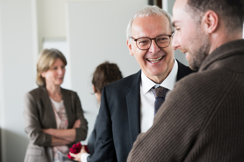 Manfred Otto-Albrecht in einem heiteren Gespräch mit Philipp Johann Trögeler. Im Hintergrund sind zwei Frauen verschwommen zu sehen.