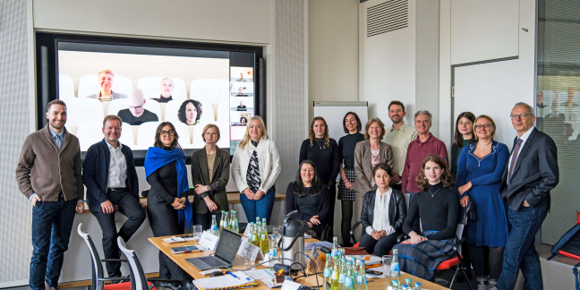 Gruppenbild mit 11 Frauen und 5 Männern von Beirat und Projekt. 4 Personen sind via Teams auf der Leinwand zu sehen.
