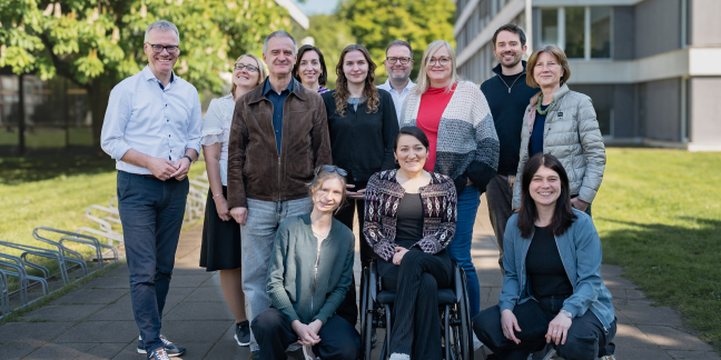 Zwölf Personen des Projekts stehen oder knien im Freien für ein Gruppenbild, eine Frau sitzt im Rollstuhl.