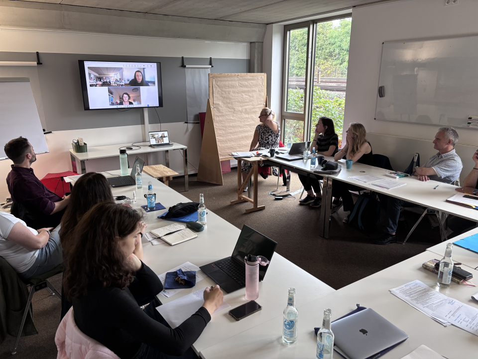 Das Team des Projekts bei der Arbeit im betahaus. Die Mitglieder an Tischen, auf einem Bildschrim sind Personen online zugeschaltet. 