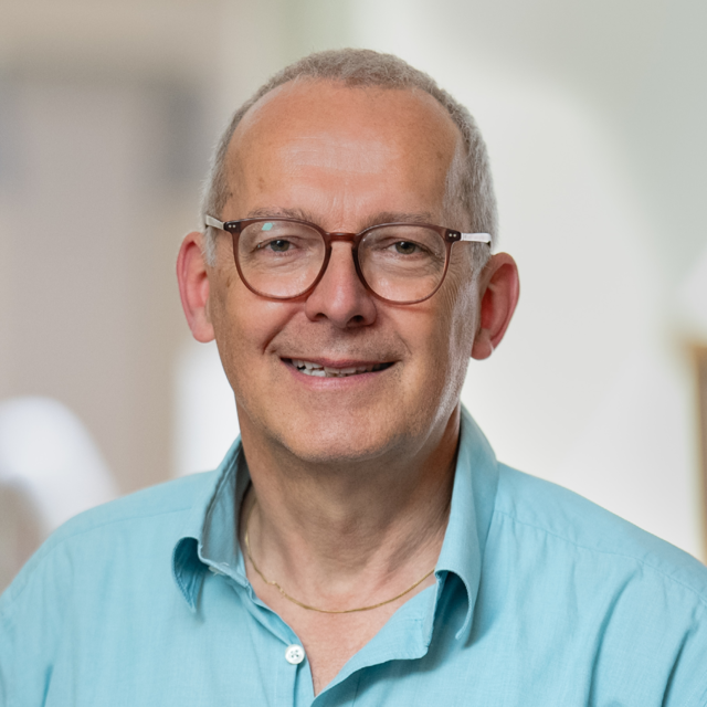 Porträt von Manfred Otto-Albrecht. Er trägt eine Brille und ein hellblaues Hemd. Der Hintergrund ist unscharf.